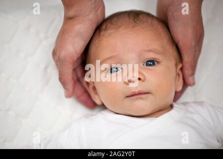 La testa del bambino dolcemente tenuti nelle mani di grandi dimensioni. Foto Stock