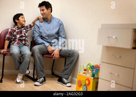 Ragazzo seduto in ospedale in sala d'attesa con suo padre. Foto Stock