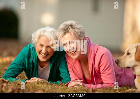 Due ridere le donne anziane che giace accanto a ogni altra in un parco Foto Stock