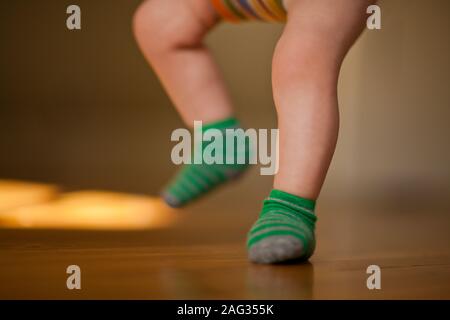 Le gambe di un bambino su un pavimento di legno mentre riversate in un ponticello di bambino. Foto Stock