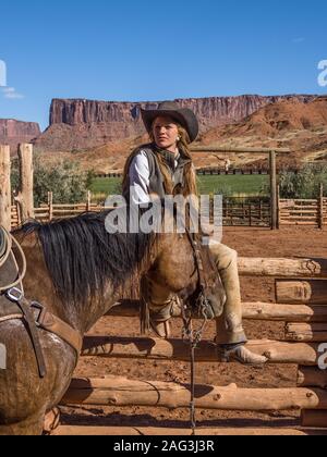 Un giovane di lavoro attraente cowgirl wrangler siede su una rampa di legno recinzione dal suo cavallo in un ranch vicino a Moab, Utah. Foto Stock