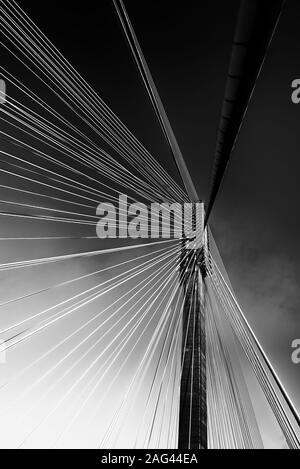 Immagine verticale in scala di grigi dei cavi di un ponte sotto bel cielo Foto Stock