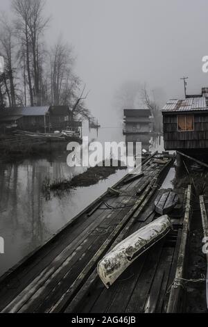 Scatto verticale di cabine di legno e pezzi di legno su la riva di un lago avvolta dalla nebbia Foto Stock