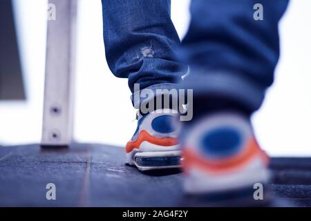 Basso angolo closeup colpo di piedi maschi in jeans e. scarpe sportive a piedi in strada Foto Stock