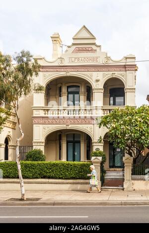 Sydney, Australia - 26 Marzo 2013: una donna cammina passato una tipica casa nei sobborghi. Questo stile architettonico era molto popolare. Foto Stock