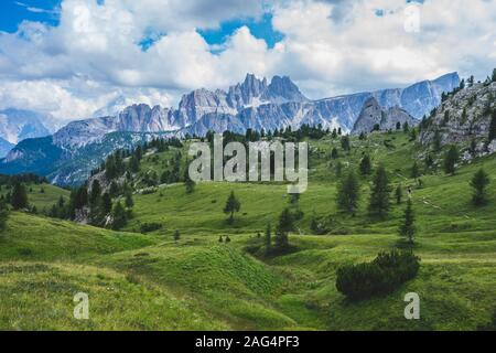 Inquadratura ad angolo basso di un campo verde circondato da montagne sotto il cielo nuvoloso delle Dolomiti Foto Stock