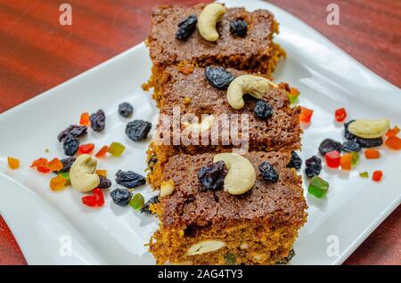 Pezzi di torta alla frutta guarnita con anacardi e uva passa nera in una piastra bianca Foto Stock