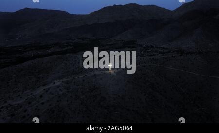 Croce illuminata nel mezzo delle montagne di notte Foto Stock