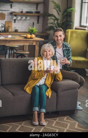 Mattina casalinga. Grey-haired anziani donna seduta sul divano con figlio Foto Stock