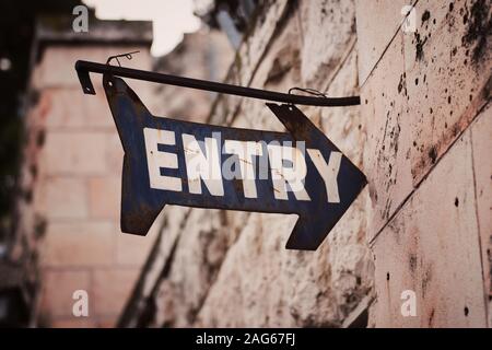 Primo piano dell'antica insegna di ingresso su un metallo arrugginito vicino ad un muro di cemento Foto Stock