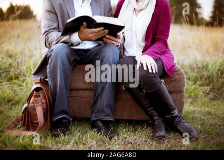 Primo piano di una coppia seduta su una valigia mentre leggere la bibbia con uno sfondo sfocato Foto Stock