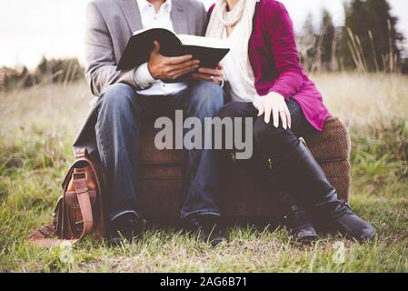 Primo piano di una coppia seduta su una valigia mentre leggere la bibbia con uno sfondo sfocato Foto Stock