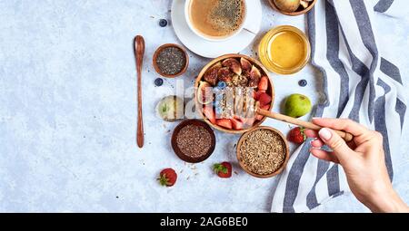 Vista dall'alto che mostra le mani di mangiare il porridge con miele, mirtilli e fragole su in legno di colore blu di sfondo tabella di buon mattino e sana prima colazione Foto Stock