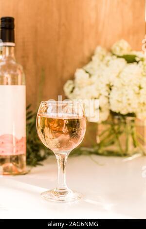 Rose blush il vino in bicchieri. Bottiglia di vino rosato con fiori su sfondo. Prosecco. Foto Stock