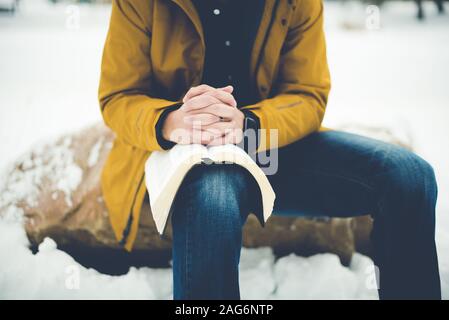 Primo piano di un maschio che indossa un jacker giallo seduto su una roccia con la bibbia sul ginocchio Foto Stock