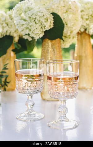 Vino rosato in bicchieri. Vino rosato sulle bottiglie d'oro dello sfondo con fiori Foto Stock