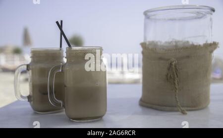 Colpo di primo piano di due milkshakes in vasi di muratore sul spiaggia su uno sfondo sfocato Foto Stock