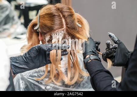 Mani in guanti neri un colorante donna capelli nel salone, la colorazione dei capelli processo. Foto Stock