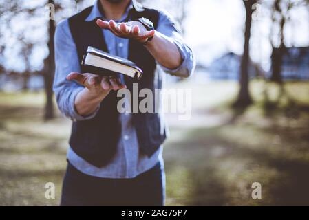 Bibbia nell'aria tra le mani di un maschio su sfondo sfocato - mostra il potere della bibbia Foto Stock