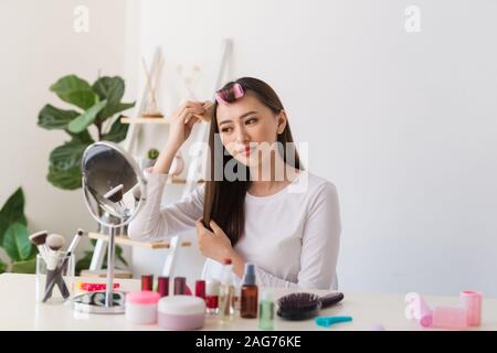 Tutorial di acconciatura. Donna asiatica spazzolare i capelli e sorridente piacevolmente durante le riprese di un tutorial per la sua bellezza blog Foto Stock