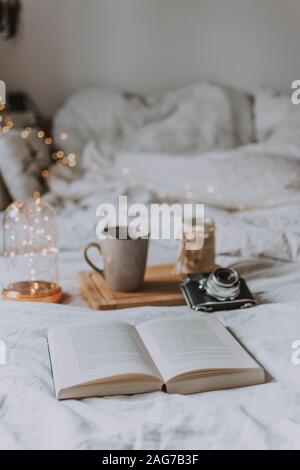 Ripresa verticale di un libro aperto, di una macchina fotografica, di un vassoio e di una tazza su un letto con fogli bianchi Foto Stock