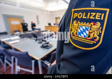 Regensburg, Germania. Xviii Dicembre, 2019. La parte convenuta (M) sorge accanto al suo avvocato in aula di tribunale regionale di fronte un poliziotto la cui camicia ha la polizia bavarese il badge cuciti su di esso. Il 51-anno-vecchio uomo è detto di avere disputato la sua auto verso due poliziotti in piedi sulla strada a Straubing in ordine per sfuggire ad un controllo del traffico. Secondo il ministero, i due ufficiali solo riusciti a salvare se stessi saltando a lato. Credito: Armin Weigel/dpa/Alamy Live News Foto Stock