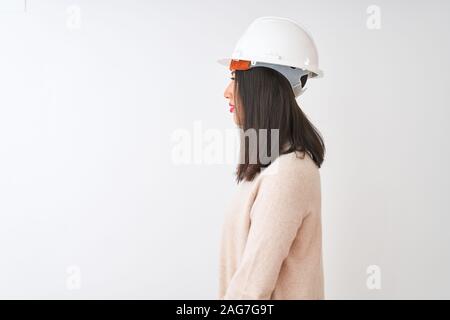 Giovane architetto cinese donna che indossa il casco di protezione isolati su sfondo bianco cercando di lato, profilo relax posano con faccia naturale con confid Foto Stock