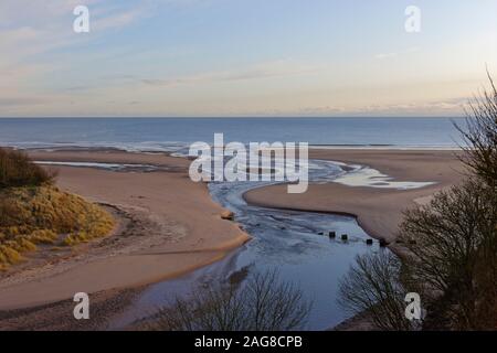 La bocca dell'acqua Lunan correndo sopra la spiaggia di Lunan Bay e nel Mare del Nord in una fredda mattina di dicembre. Foto Stock