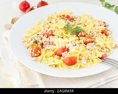 Farfalle con pasta al pomodoro, carne di pollo, prezzemolo in pietra bianca di sfondo, dieta ipocalorica, la vista laterale Foto Stock