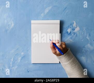 Donna scrive in notebook su una pietra tavolo blu, mano nella camicia tenendo una matita, sketchbook disegno, vista dall'alto Foto Stock
