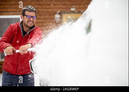 Uomo che indossa una giacca rossa e che tovana la neve con un sfondo sfocato Foto Stock