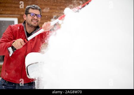 Uomo che indossa una giacca invernale rossa e pulisce la neve fuori dall'auto Foto Stock