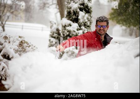 Primo piano di un maschio che indossa una giacca invernale rossa durante la pulizia della neve dall'auto Foto Stock