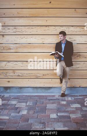 Scatto verticale di un maschio ben vestito appoggiato al muro durante la lettura della bibbia Foto Stock