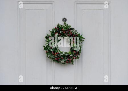 Un Natale Holly corona appeso a un legno bianco dello sportello anteriore Foto Stock