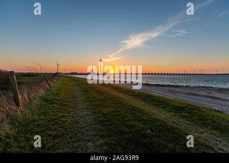 Una barriera contro le tempeste e mulini a vento nella provincia di Zeeland in I Paesi Bassi al tramonto Foto Stock