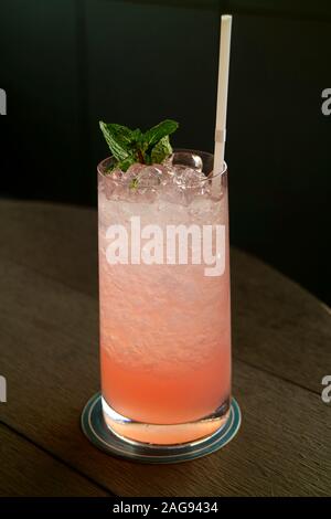 Foto verticale di un bicchiere di Coral Pink cocktail sul tavolo di legno Foto Stock