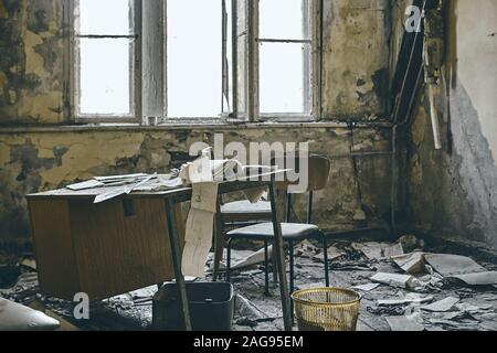 Scatto drammatico di una casa abbandonata con muri distrutti e. libri di tempo sul vecchio tavolo Foto Stock