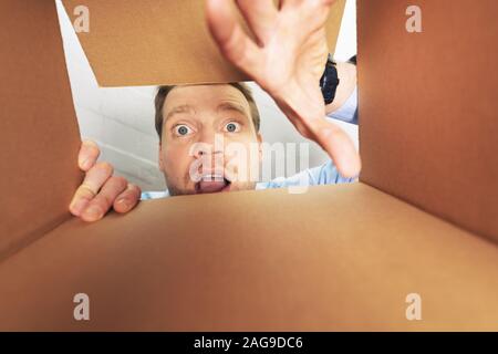 Uomo eccitato per aprire la scatola di cartone e guardando all'interno Foto Stock