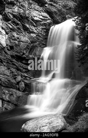 Immagine verticale in scala di grigi di una cascata vicino alle scogliere in una foresta Foto Stock