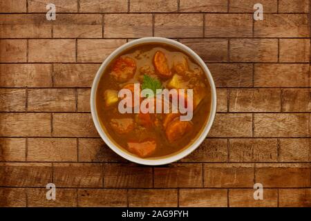 Una tazza di delizioso inverno sostanziosa zuppa di verdure, in una ciotola rustico, su un verificato uno sfondo di legno. Foto Stock