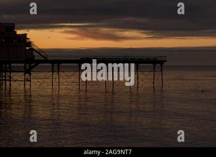 Per gli storni posatoio sotto il Vittoriano molo sul mare come il sole tramonta in Aberystwyth con un nuotatore solitario in mare Foto Stock