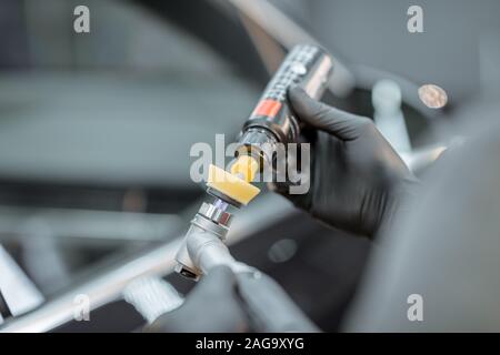 Lavoratore di guanti protettivi applicare cera su una smerigliatrice per carrozzeria di auto lucidatura, close-up. Auto professionali concetto dettagliato Foto Stock