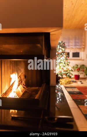 Legna da ardere all'interno di un camino con l'albero di Natale decorato sullo sfondo Foto Stock