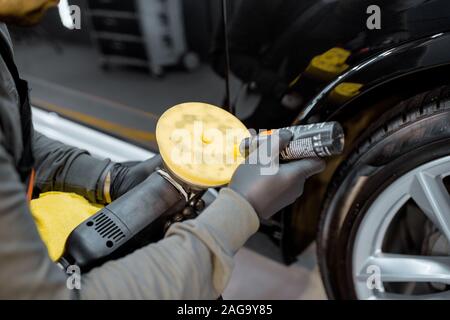 Lavoratore di guanti protettivi applicare cera su una smerigliatrice per carrozzeria di auto lucidatura, close-up. Auto professionali concetto dettagliato Foto Stock