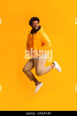 Gioiosa afro ragazzo in giacca calda del salto in aria Foto Stock