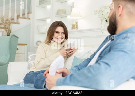 Giovane donna utilizzando phone, uomo dando massaggio piedi alla moglie Foto Stock