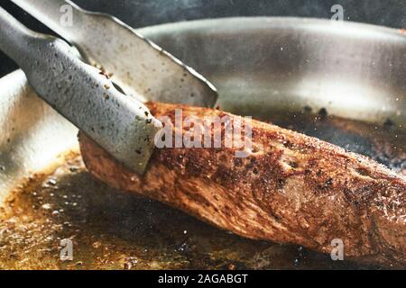 La cottura di carni bovine in un ristorante. bistecca e chef. closeup pezzo di carne arrosto Foto Stock