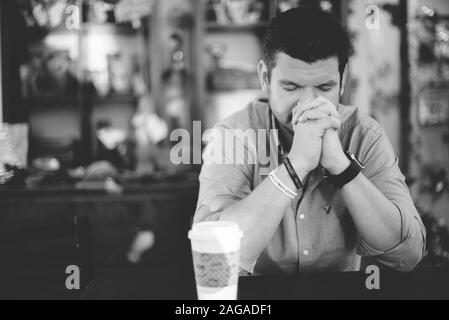 Immagine in scala di grigi di un maschio seduto nel caffè e. pregare Foto Stock