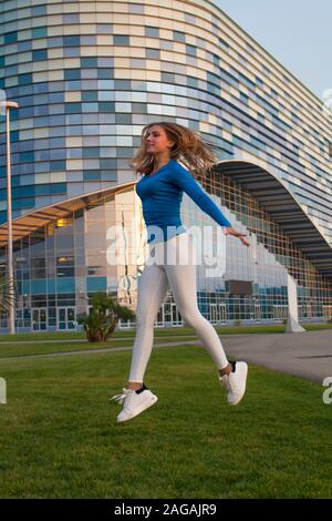 Atletico e ragazza flessibile impegnata in atletica leggera sullo sfondo della città, ella jumping Foto Stock